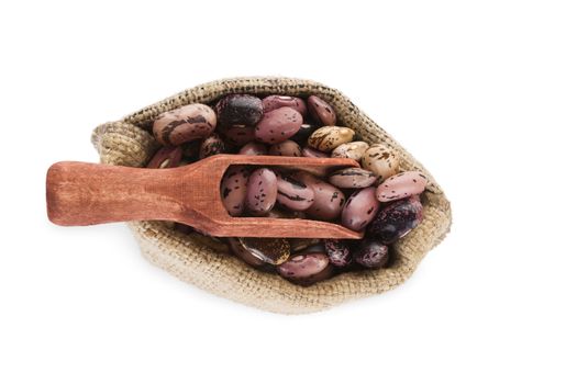 Pinto beans in burlap bag with wooden scoop isolated on white background, top view. Healthy legume eating.