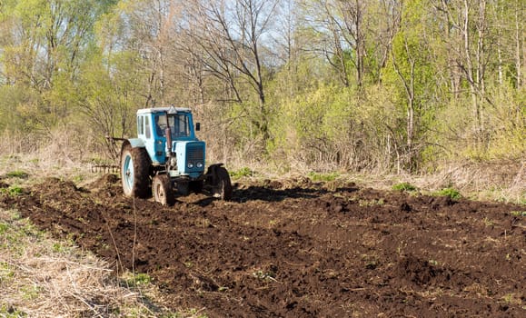 Blue tractor plowing a field in spring
