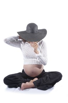 eight months brunette pregnant woman bare tummy belly button wool top sweater black trousers big pamela hat posing as fashion model isolated on white