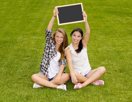 Tennage students sitting on the grass and holding a chalkboard