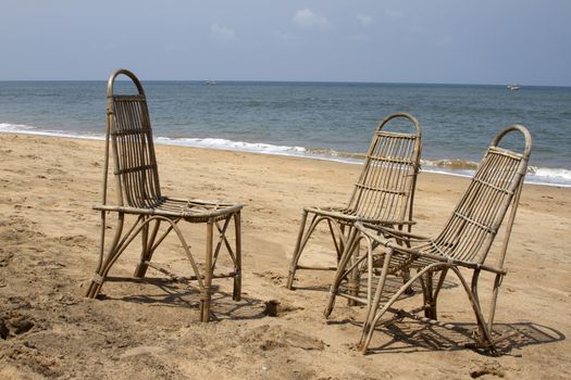 Three wattled chairs stand on a beach, wait for people against the sea. GOA India beach.