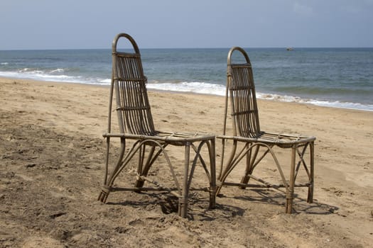 Two wattled chairs stand on a beach, wait for people against the sea. GOA India beach.