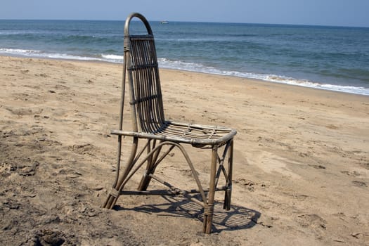 The lonely wattled chair costs on a beach, against the sea. GOA India beach.