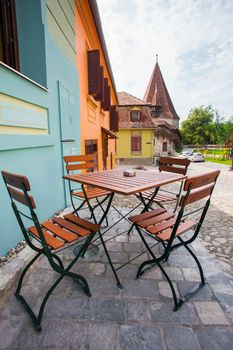 Sighisoara, Romania - June 23, 2013: Table with chairs on stone paved old street and colored houses from Sighisoara fortresss, Romania