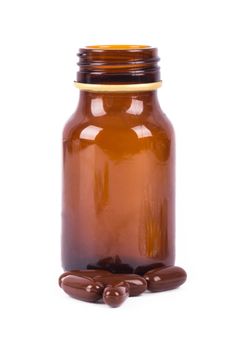 Close-up brown pills in front of medical bottle, isolated on white background.