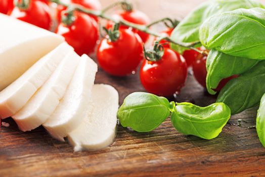 Ingredients for Caprese salad with mozzarella, tomato, basil and balsamic vinegar arranged on wooden table