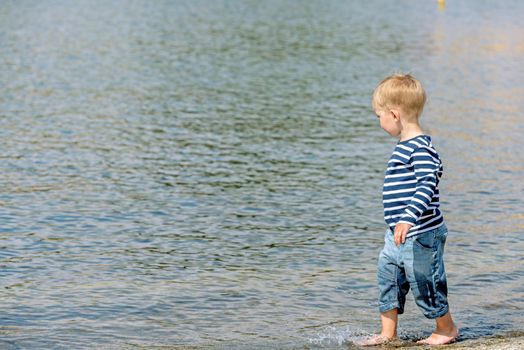 Little preschool boy walking on shore outdoors