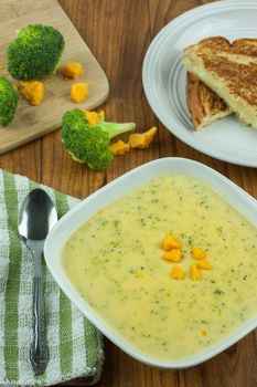 Broccoli cheese soup in a white bowl with a grilled cheese sandwich on a wooden table.