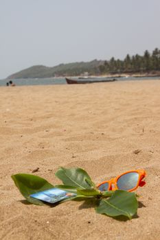 Orange sunglasses and bank cards lying on the sand beach. India Goa.