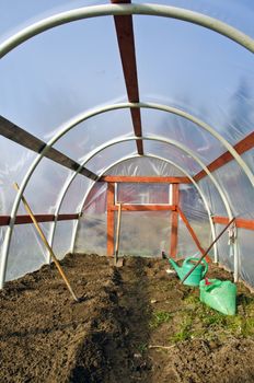 early spring time greenhouse inside construction with gardener tools and earth soil