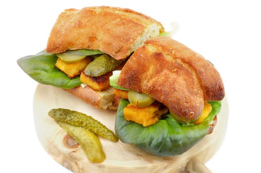 Homemade Fish Burgers with  Fish Sticks, Gherkins, Lettuce, Tartar Sauce and Whole Wheat Bread on Circle Wooden Cutting Board closeup on white background