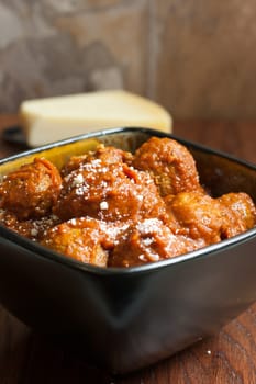 Itailian meatballs and marinara sauce in a bowl with a block of fresh Parmesan cheese in the background.
