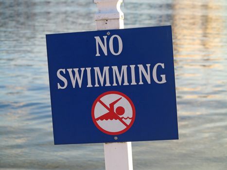 A sign showing no swimming in the water behind