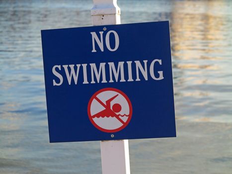 A sign showing no swimming in the water behind