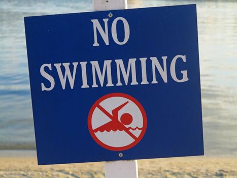 A sign showing no swimming in the water behind