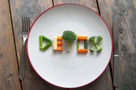 Detox text on a plate made from various vegatables including broccoli, spring onions and carrots