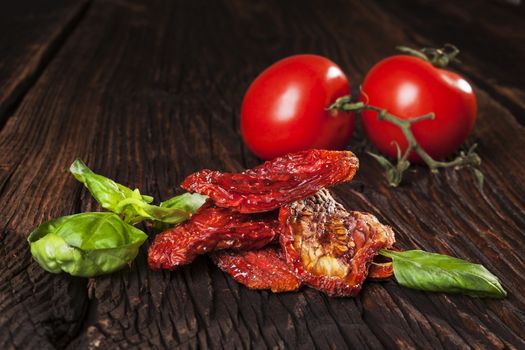 Delicious dried tomatoes, fresh ripe tomatoes and basil on brown wooden vintage textured background. Traditional mediterranean kitchen.