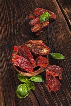 Delicious dried tomatoes and fresh basil herbs in wooden bowl on brown wooden vintage textured background. Traditional mediterranean kitchen.
