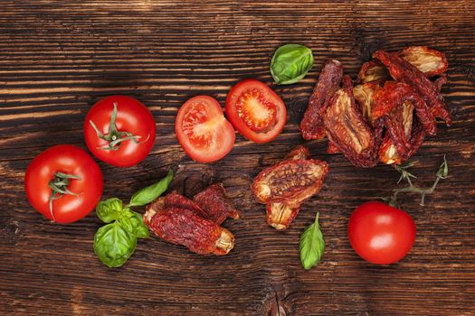 Delicious sundried, fresh tomatoes and basil herbs on brown wooden vintage textured background, top view. Traditional mediterranean kitchen.