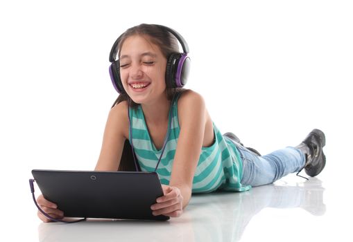 Beautiful pre-teen girl on the floor, usin a tablet computer and headphones, white background