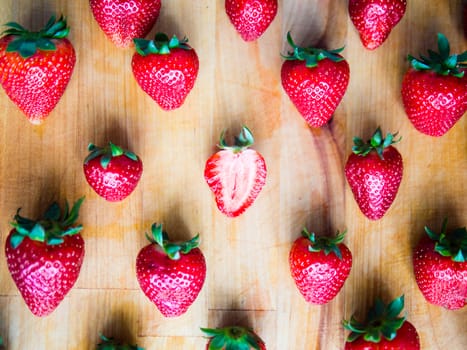 One cutted strawberry in an srranged pattern of strawberries on a wooden board, difference expression