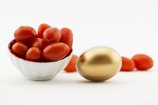 Cherry tomatoes placed with gold egg on white background with copy space available.  Metaphors suggest fresh agriculture, local produce, farm industry, restaurant business, ogranic foods, are successful investments.  Healthy diet and nutrition pay off. 