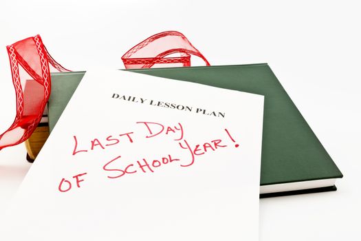 Teacher's daily lesson plan sheet marked with "Last Day of School" placed with books and festive red ribbon