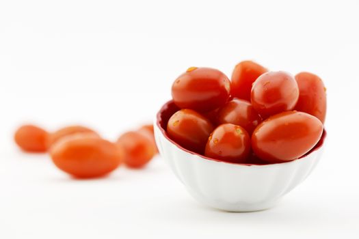 Selective focus on red cherry tomatoes in small white dish with crimson interior; copy space available on horizontal image.  Shallow depth of field results in loose cherry tomatoes in background being out of focus. Damp droplets on produce. 