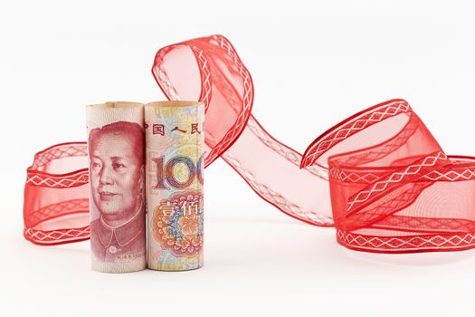 Yuan currency stands upright in front of swirl of red ribbon on white background in horizontal image.  