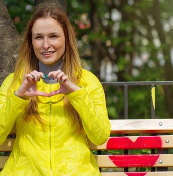 Girl folded her fingers in the form of heart. On a bench in the park
