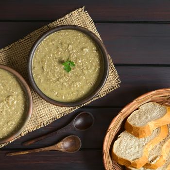 Cream of lentil soup in rustic bowl with wooden spoons and bread slices in basket on the side, photographed overhead on dark wood with natural light