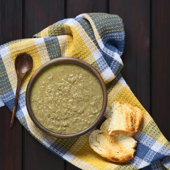 Cream of lentil soup in rustic bowl with wooden spoon and toasted bread slices on kitchen towel, photographed overhead on dark wood with natural light