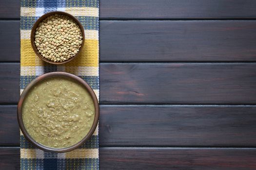 Cream of lentil soup in rustic bowl and raw lentils in small bowl on kitchen towel, photographed overhead on dark wood with natural light