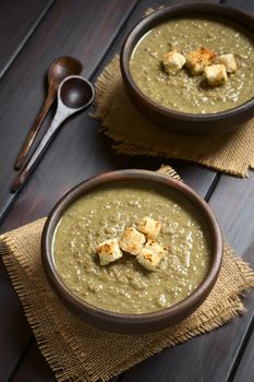 Cream of lentil soup in rustic bowls with croutons on top, wooden spoons on the side, photographed on dark wood with natural light (Selective Focus, Focus on the front of the croutons on the first soup)