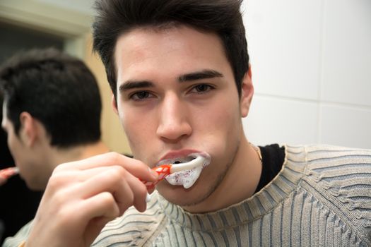 Headshot of attractive young man brushing teeth with toothbrush, looking at camera Headshot of attractive young man brushing teeth with toothbrush, looking at camera