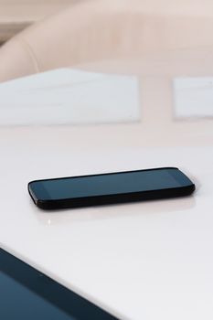 Black mobile phone with blank black screen on white table.