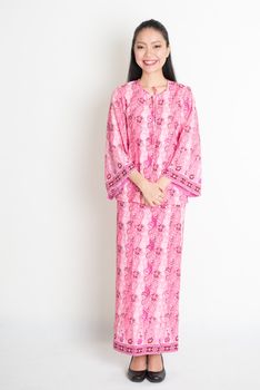 Full body portrait of happy Southeast Asian girl in pink batik dress standing on plain background.
