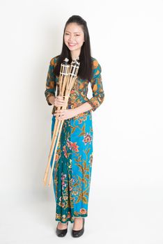 Full body portrait of Southeast Asian girl in batik dress hands holding pelita standing on plain background.