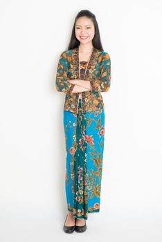 Full body Southeast Asian girl in batik dress standing on plain background.