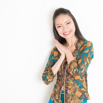 Portrait of happy Southeast Asian woman in batik dress on plain background.
