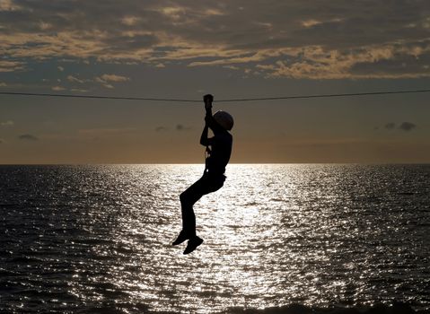 silhouette of young girl on zip line in summer sundown 