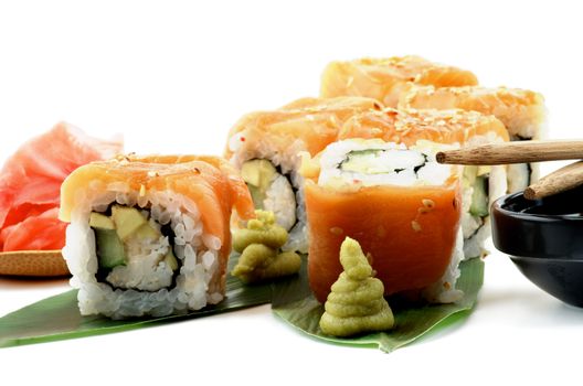 Maki Sushi with Salmon, Crab, Avocado and Cheese on Green Palm Leafs with Wasabi, Ginger and Pair of Chopsticks closeup on White background