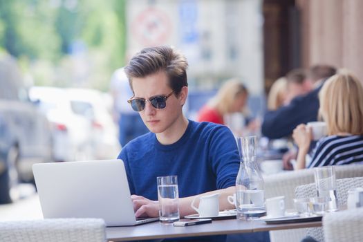 Young Man with Laptop Sitting in Outside Coffeehouse Working