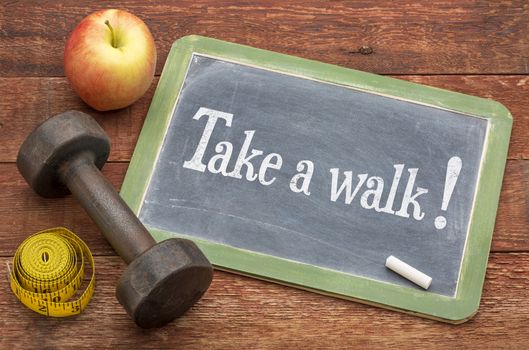 take a walk - fitness concept -  slate blackboard sign against weathered red painted barn wood with a dumbbell, apple and tape measure