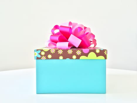 Blue gift box with pink ribbon, on white table.