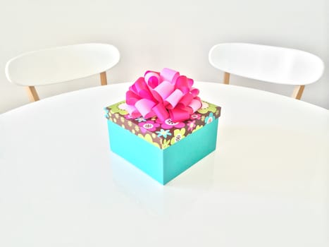 Colorful gift box with pink ribbon, on white table.