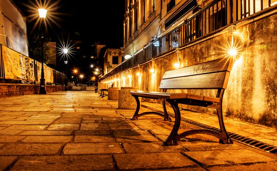 Night scene with bench on paved, narrow street.