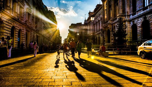 People in sunlight with long shadows on Lipscani Street, Bucharest.