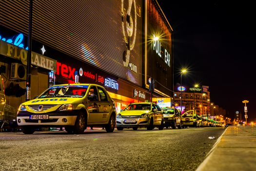 A line of taxi cars in front of shopping center, in Bucharest at night.