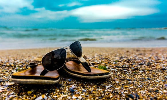 Slippers and sunglasses on the shore with sand and sea water